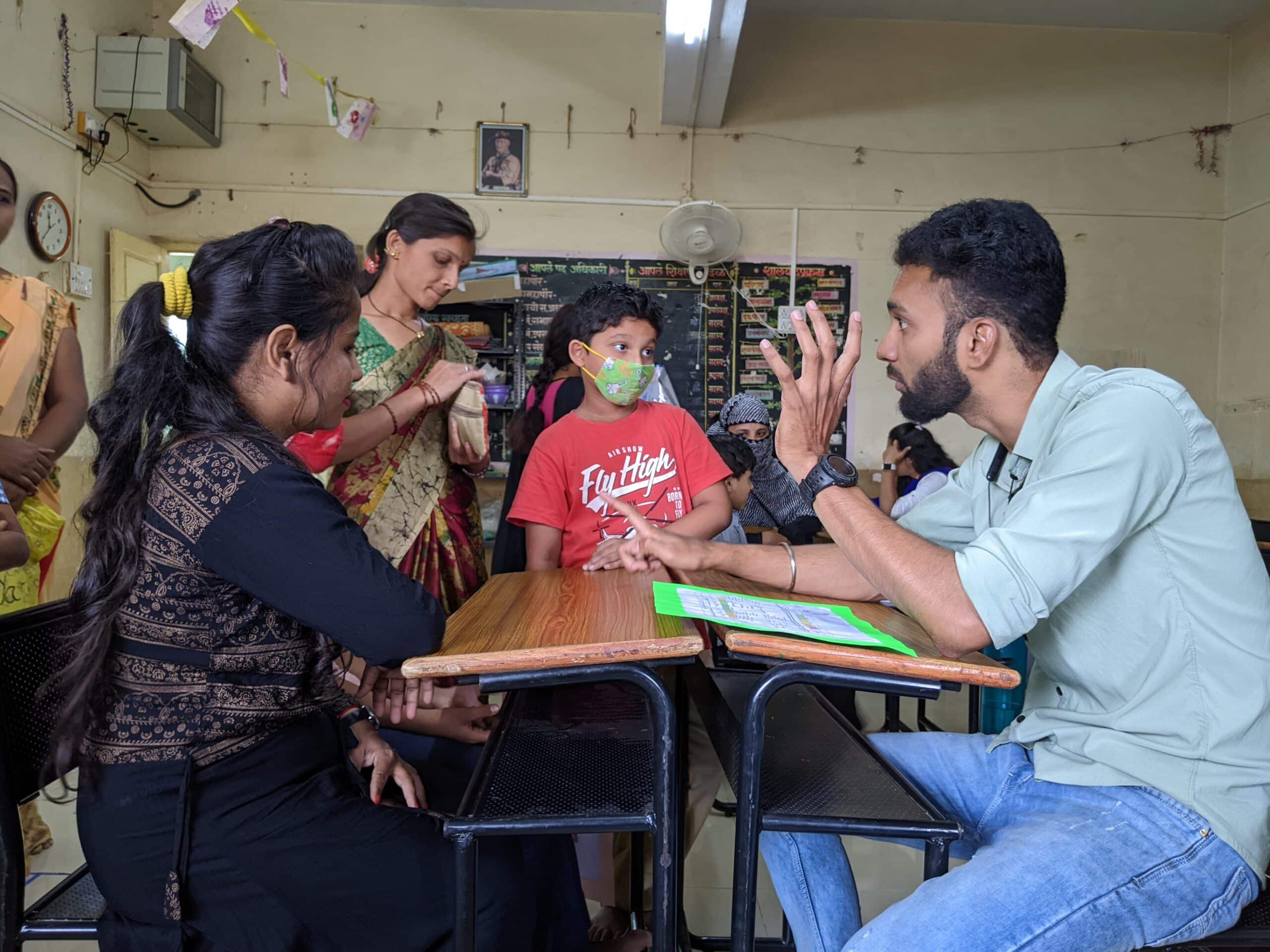 Children gathering around school desk while teacher explains something to them.