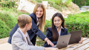 Three students talking while pointing to content on a laptop screen on school courtyard