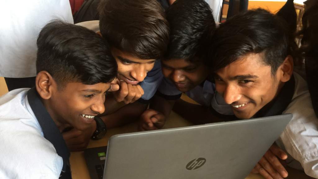 Students sitting closely all around the same laptop