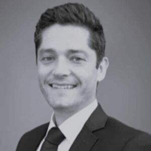 Professional headshot of a man in a suit smiling against a neutral background