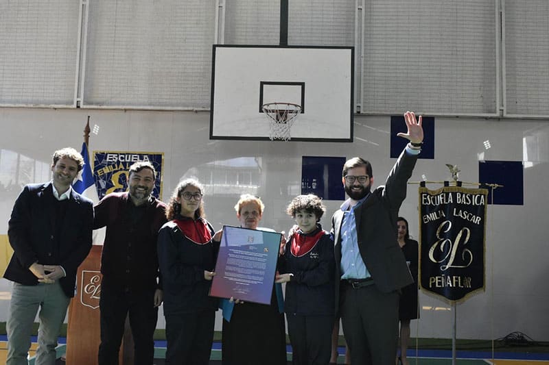 President Gabriel Boric with a group celebrating at Escuela Emilia Lascár, holding a certificate in a gymnasium.