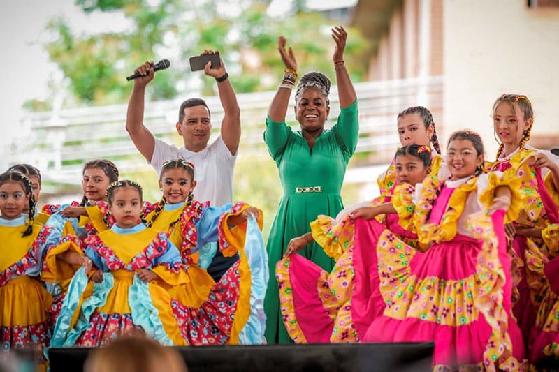 Children dressed in vibrant traditional Colombian attire performing a cultural dance outdoors.