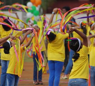Children performing a ribbon dance in yellow outfits during a colorful celebration.