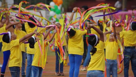 Children performing a ribbon dance in yellow outfits during a colorful celebration.