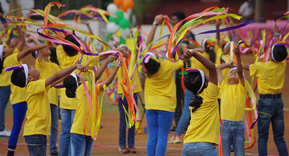 Children performing a ribbon dance in yellow outfits during a colorful celebration.