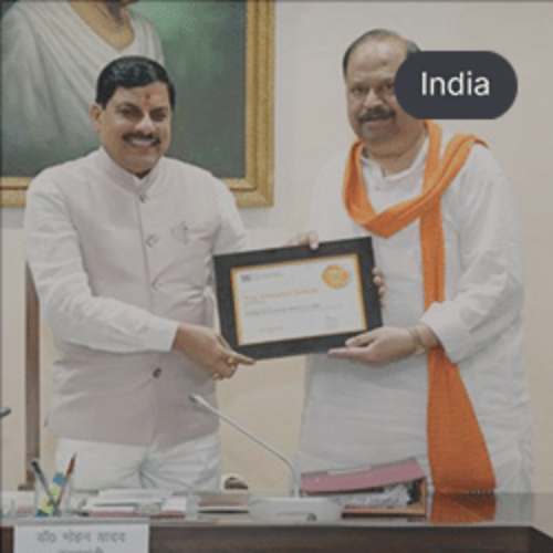 Two officials smiling and holding a framed certificate during a formal event in an office setting.