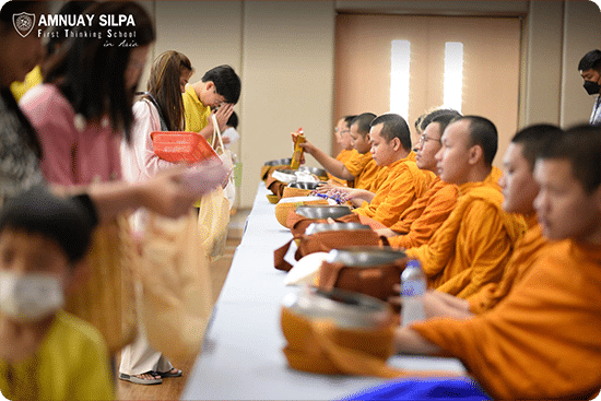 Students and teachers presenting offerings to monks during a Buddhist almsgiving ceremony at school.
