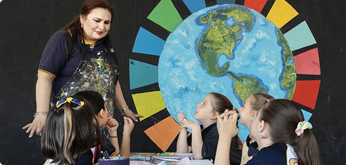 Teacher engaging with young students in front of a painted Earth and colorful design representing unity
