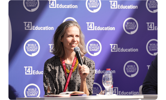 A smiling speaker holding a microphone during a panel discussion at the World Schools Summit, with event branding in the background.