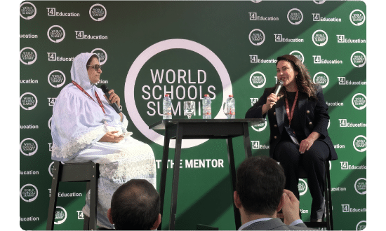 Two speakers engaging in a one-on-one conversation on stage at the World Schools Summit, with an audience observing.