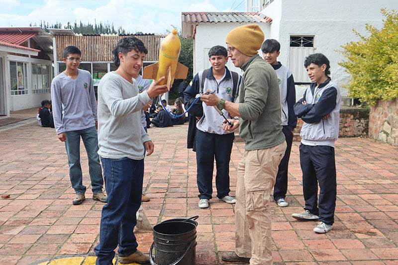 Students and a teacher preparing a small model rocket for a science experiment in a school courtyard