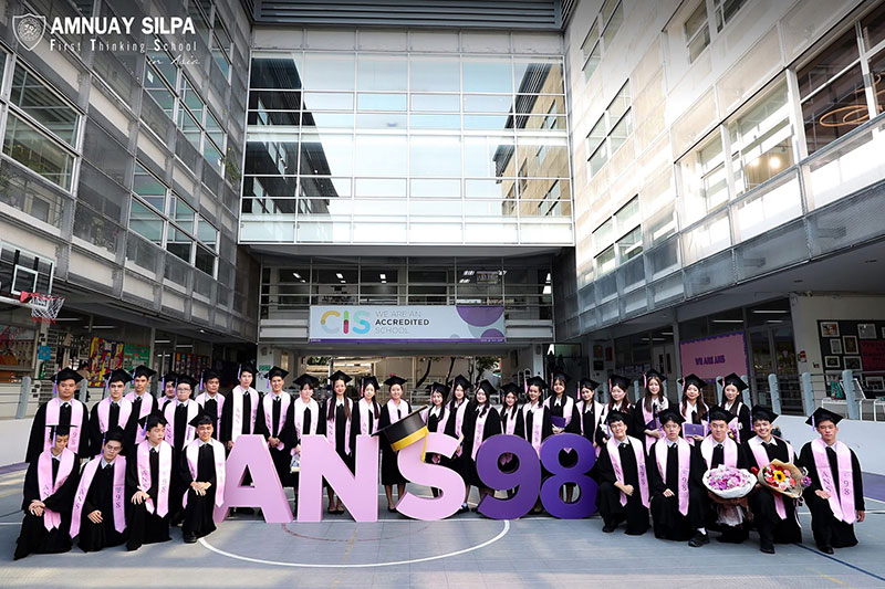 Graduating students posing in front of a school building with large letters and numbers reading 