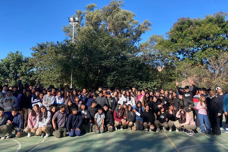 Large group of students and teachers gathered on a school basketball court surrounded by trees