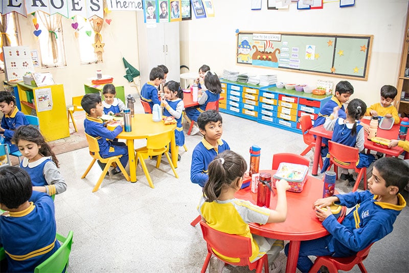 Young students sitting at colorful round tables having lunch in a classroom
