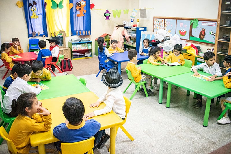 Early learners engaged in reading activities at colorful classroom tables