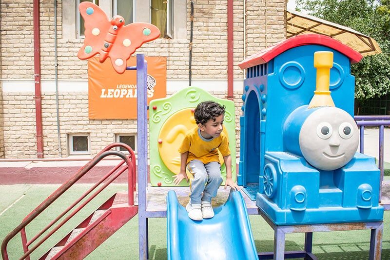 A young child playing on colorful playground equipment shaped like a train