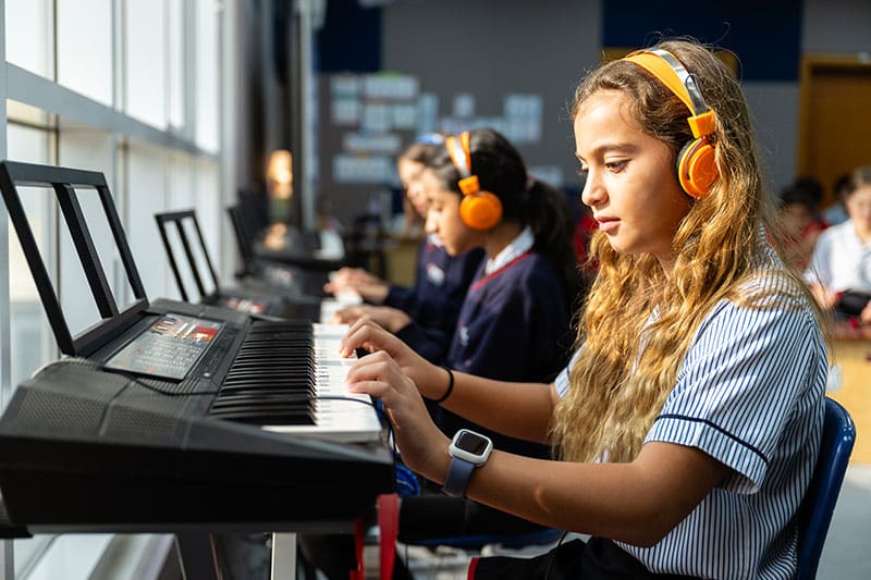 Student wearing headphones playing an electric keyboard in a music class
