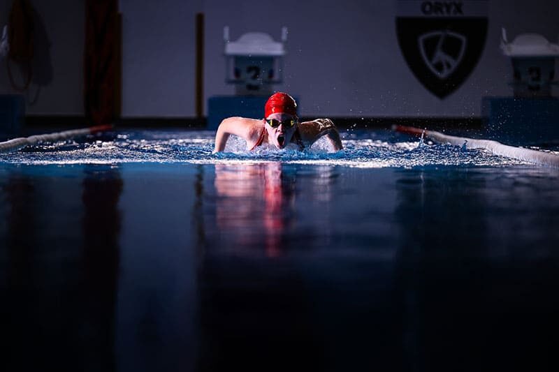 Swimmer in red cap mid-stroke during a race in an indoor pool