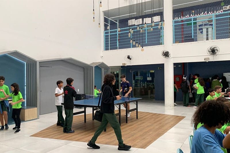 Students at Escola COC São Luís playing table tennis and socializing during break in the school lobby.