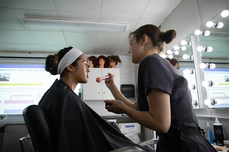 Student receiving makeup application in school vocational salon setting