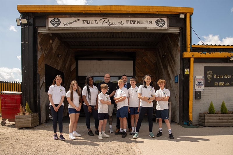 Group of students and coach standing outside a local gym, wearing academy uniforms