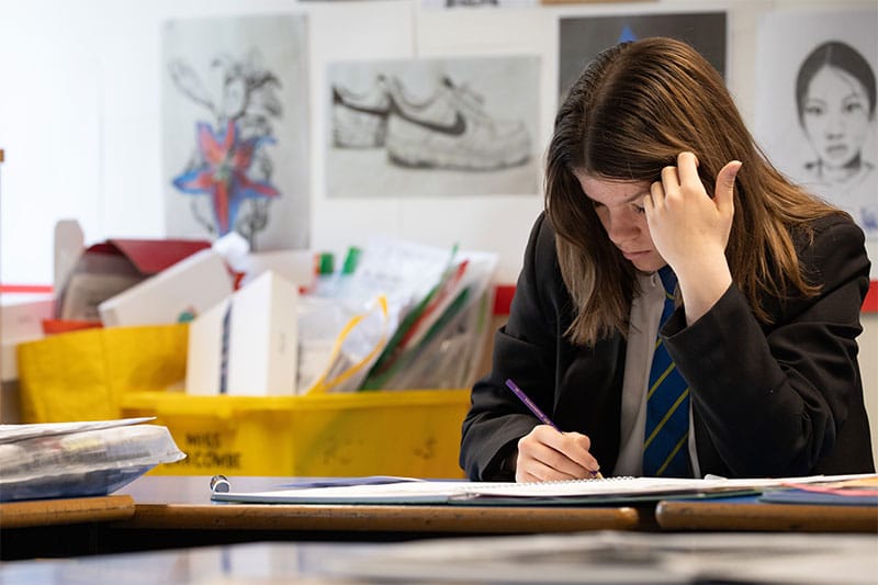 Student focused on drawing in an art classroom filled with sketches