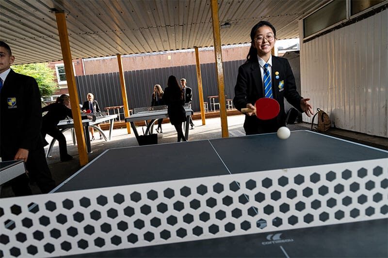 Student in school uniform playing table tennis in a covered outdoor area