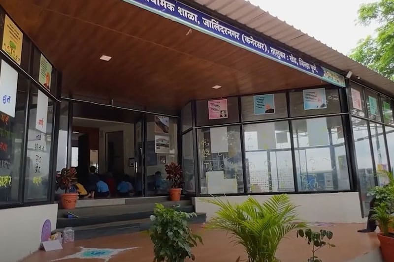 Entrance of The School Jalindarnagar with glass walls, potted plants, and educational posters
