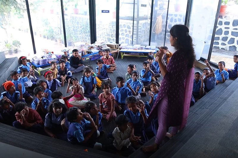 Teacher leading an interactive activity with a group of young students seated on tiered steps at The School Jalindarnagar