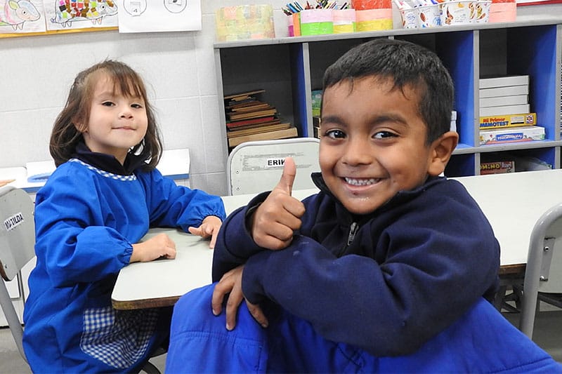 Young boy giving a thumbs up and smiling next to a classmate in a colourful classroom