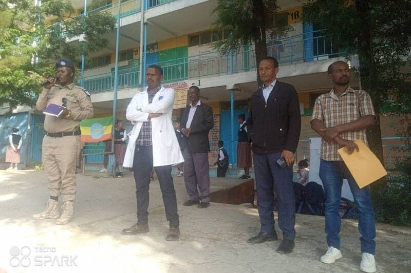 School staff and a local officer speaking to students in front of a classroom building