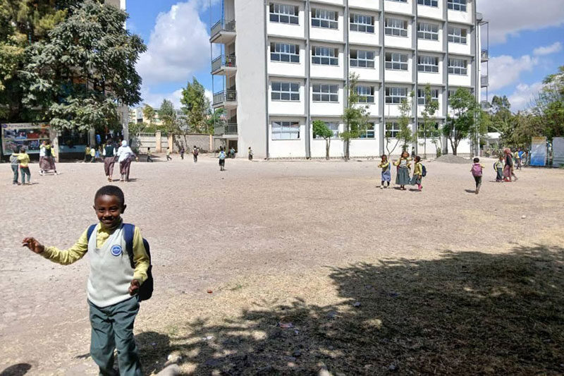 Smiling student in school uniform walking across an open courtyard with a school building in the background