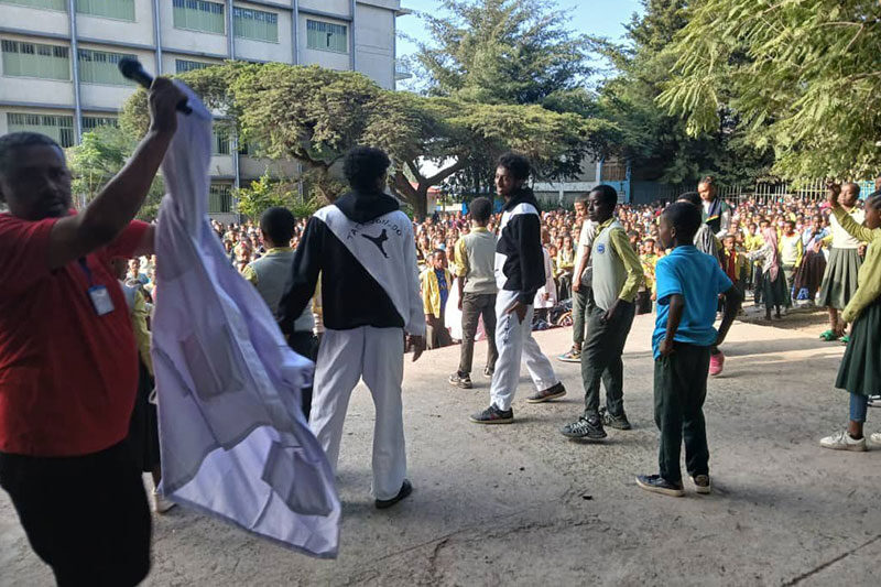 Students performing on stage while a crowd of peers watches in a school courtyard