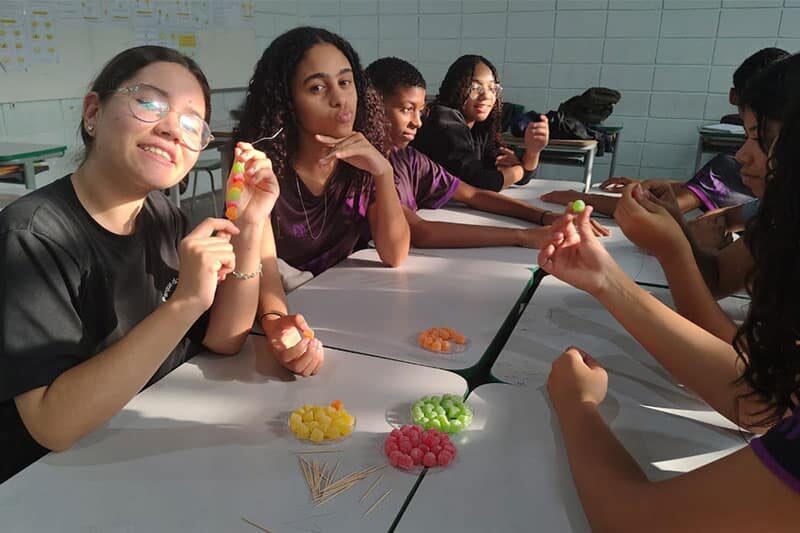 Students sitting at classroom tables working on a hands-on activity using colourful sweets and toothpicks, smiling and engaging creatively.