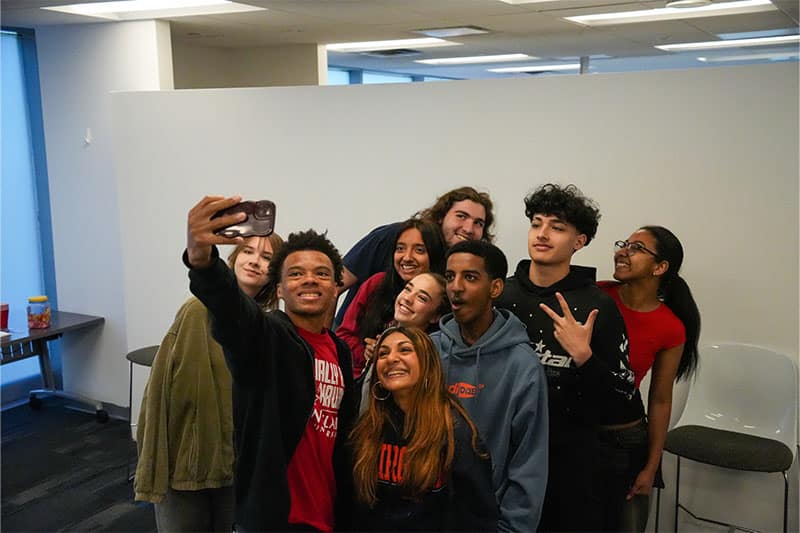 Group of smiling teenagers taking a selfie together in a modern indoor space.