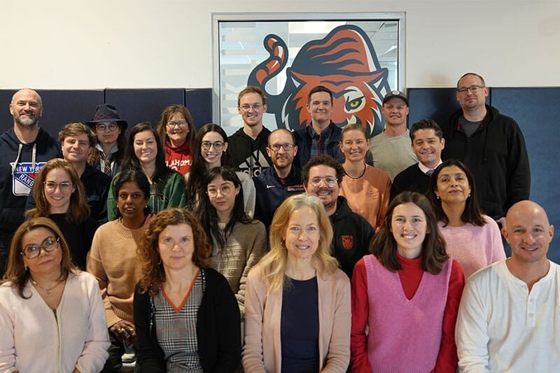 Group of adults posing together for a group photo indoors, with a large tiger logo in the background.