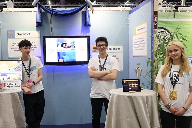 Three young individuals stand at a technology exhibition booth showcasing a project called 