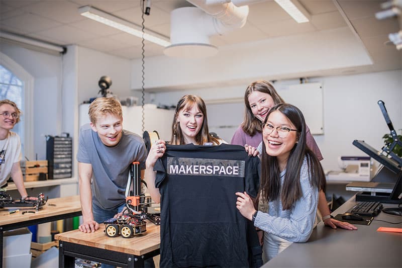 Group of students in a makerspace holding a T-shirt with the word Makerspace printed on it