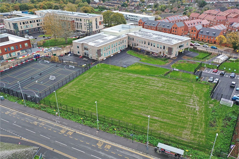 Aerial view of a modern school campus featuring classroom buildings, sports courts, a football field, and surrounding residential neighbourhood.