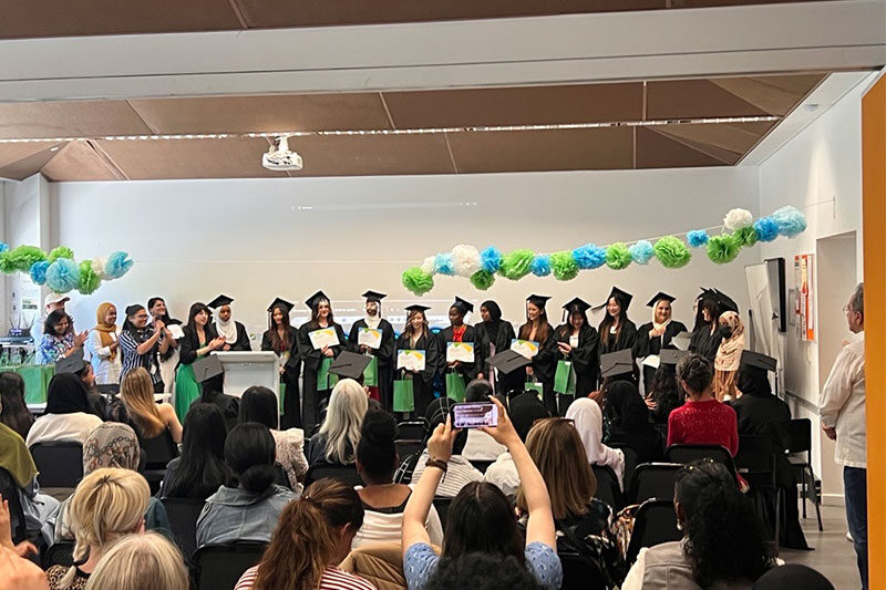 Graduates in caps and gowns holding certificates during a ceremony, with audience watching