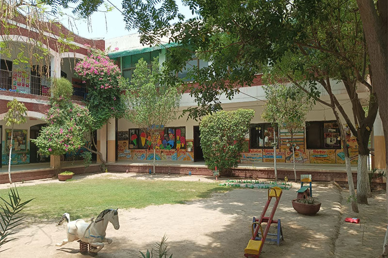 School courtyard with playground equipment, trees, and colourful classroom walls