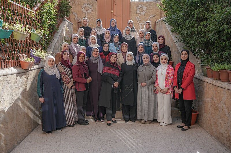 Group of women standing together on an outdoor staircase, posing for a formal group photo in a courtyard with plants and decorative walls.