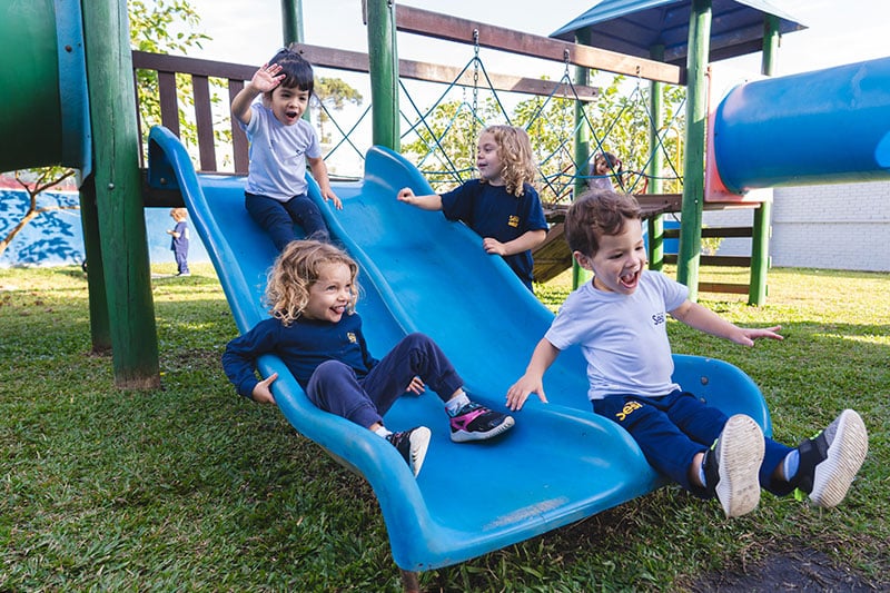 Young children playing and sliding down a blue slide on a playground structure