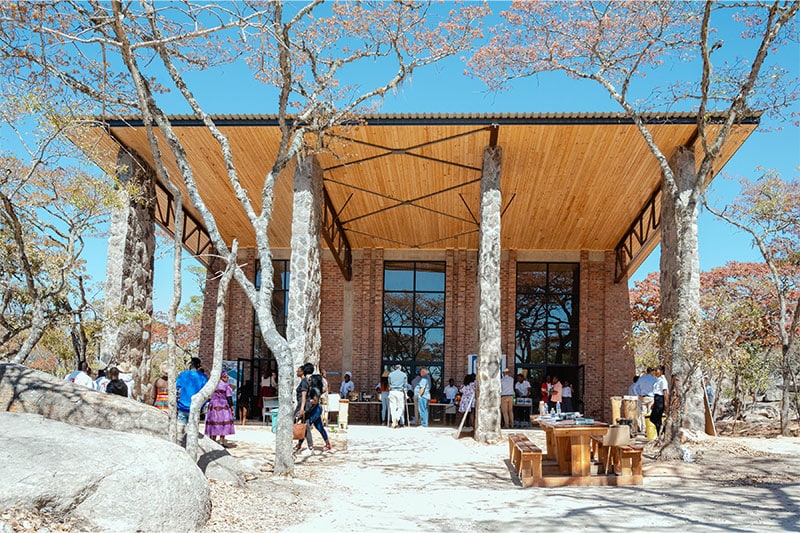 Modern building with tall trees integrated into its open design, surrounded by people in a natural, wooded setting.