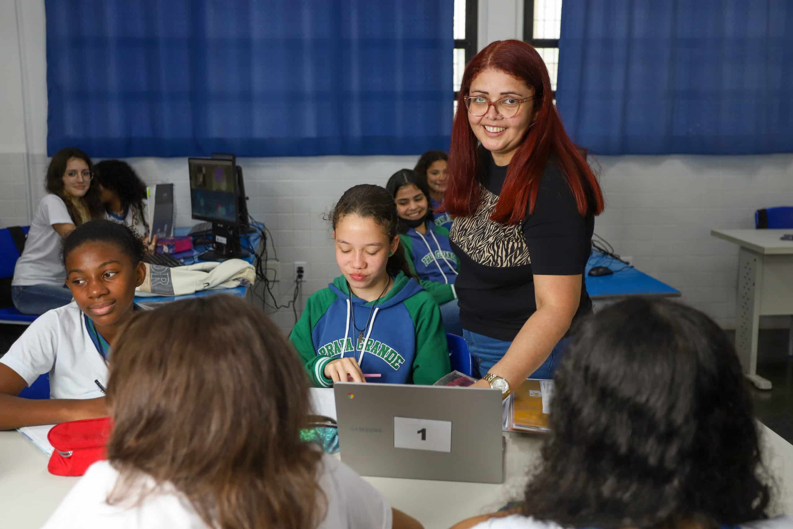Teacher assisting middle school students working on laptops in a computer lab classroom