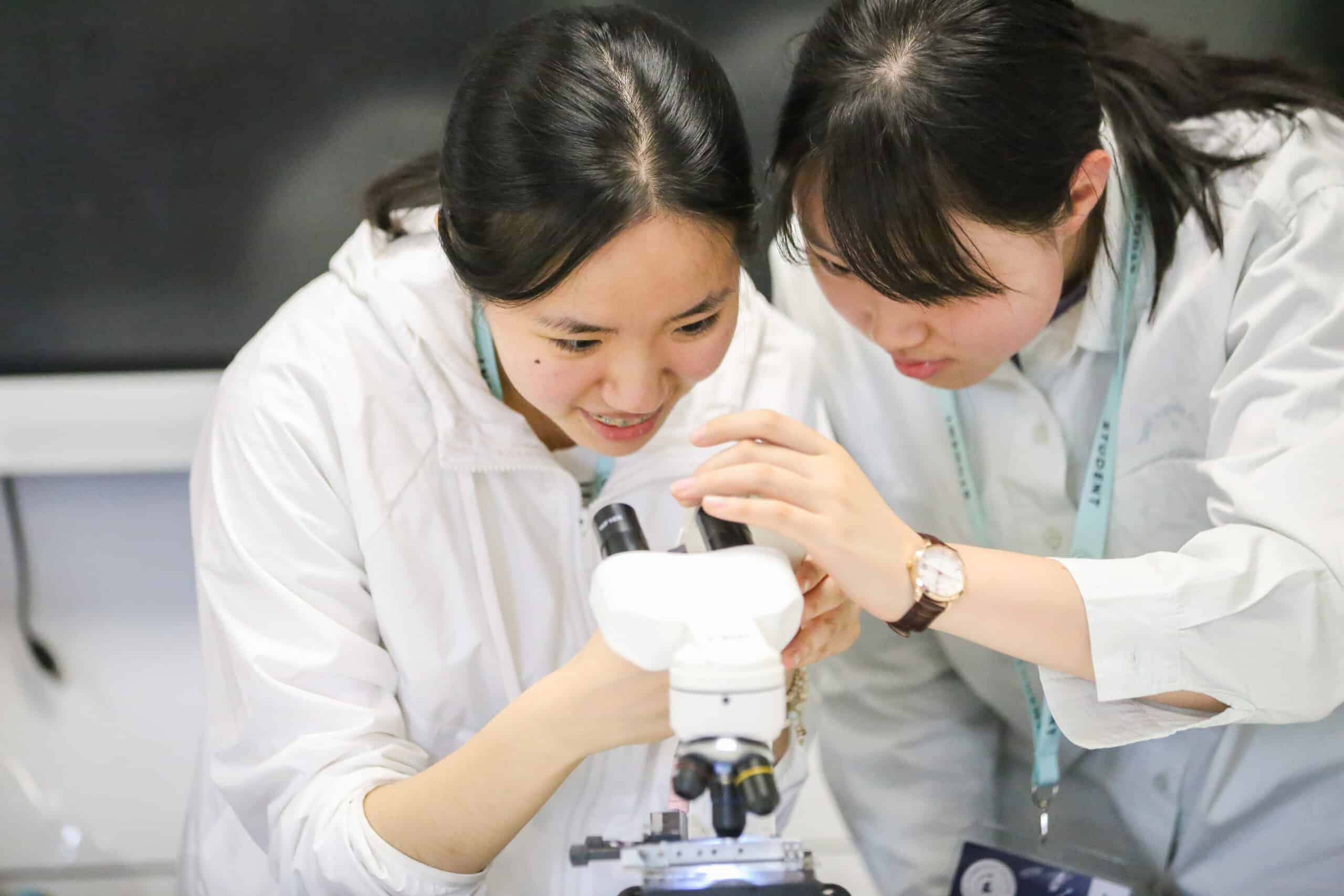 Two students observing a microscope together in a lab setting.