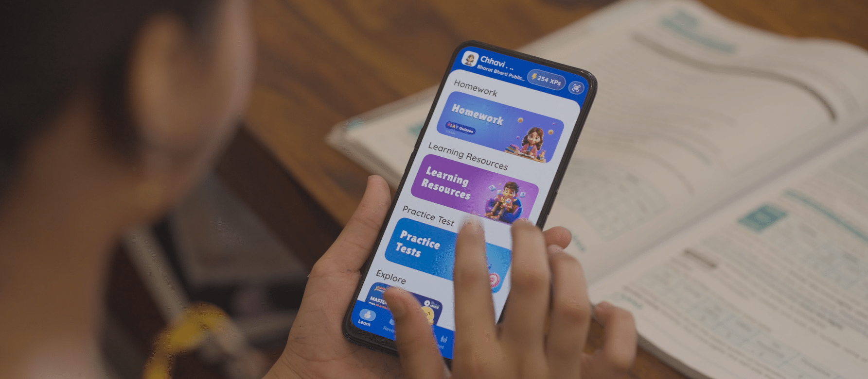 A person interacting with a learning app on their phone, with an open textbook in the background.
