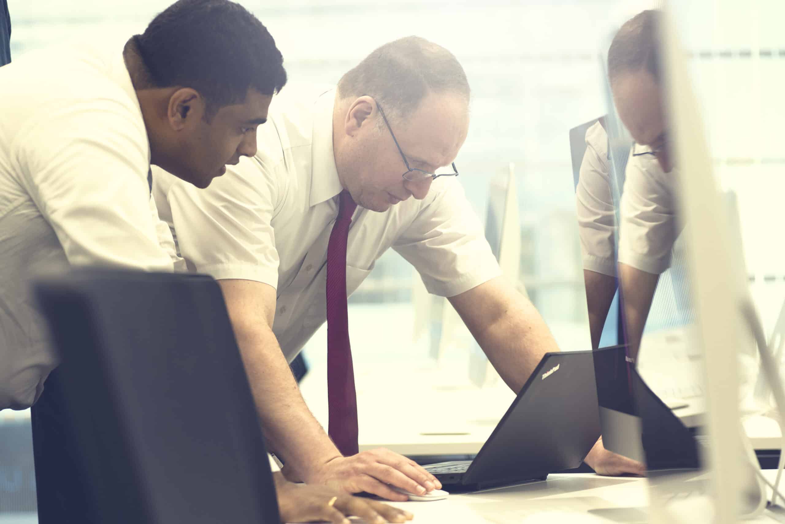 Two professionals in business attire collaborating while looking at a laptop in a modern office setting