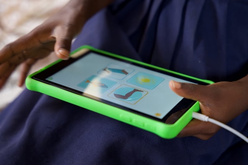 Child using a tablet with educational icons on screen, held in a green protective case