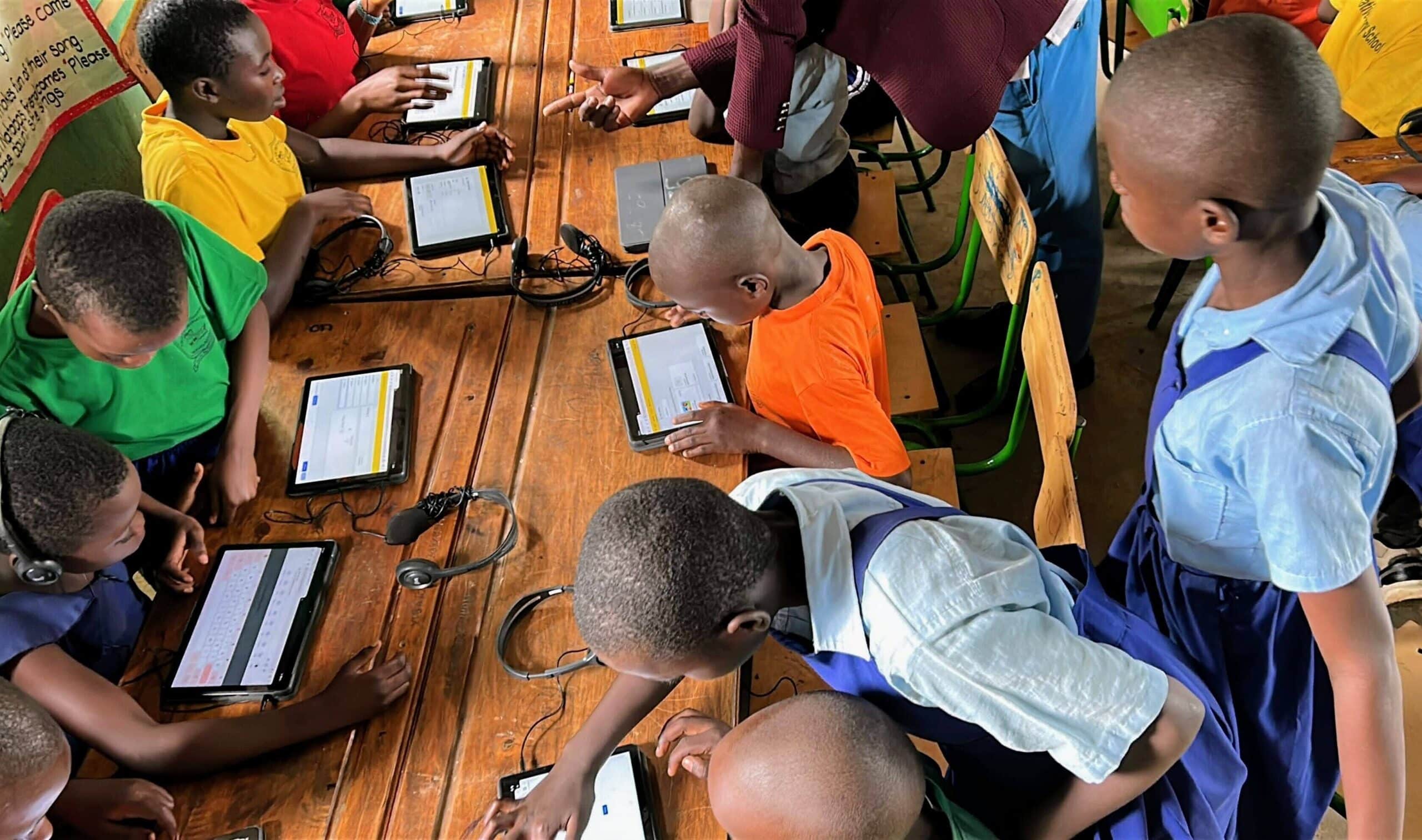 Group of young students using tablets with headsets in a classroom, guided by a teacher at a wooden table